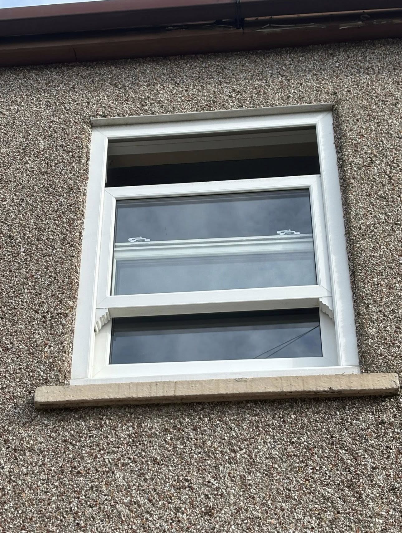 White uPVC sliding sash window partially open on a pebbledash facade