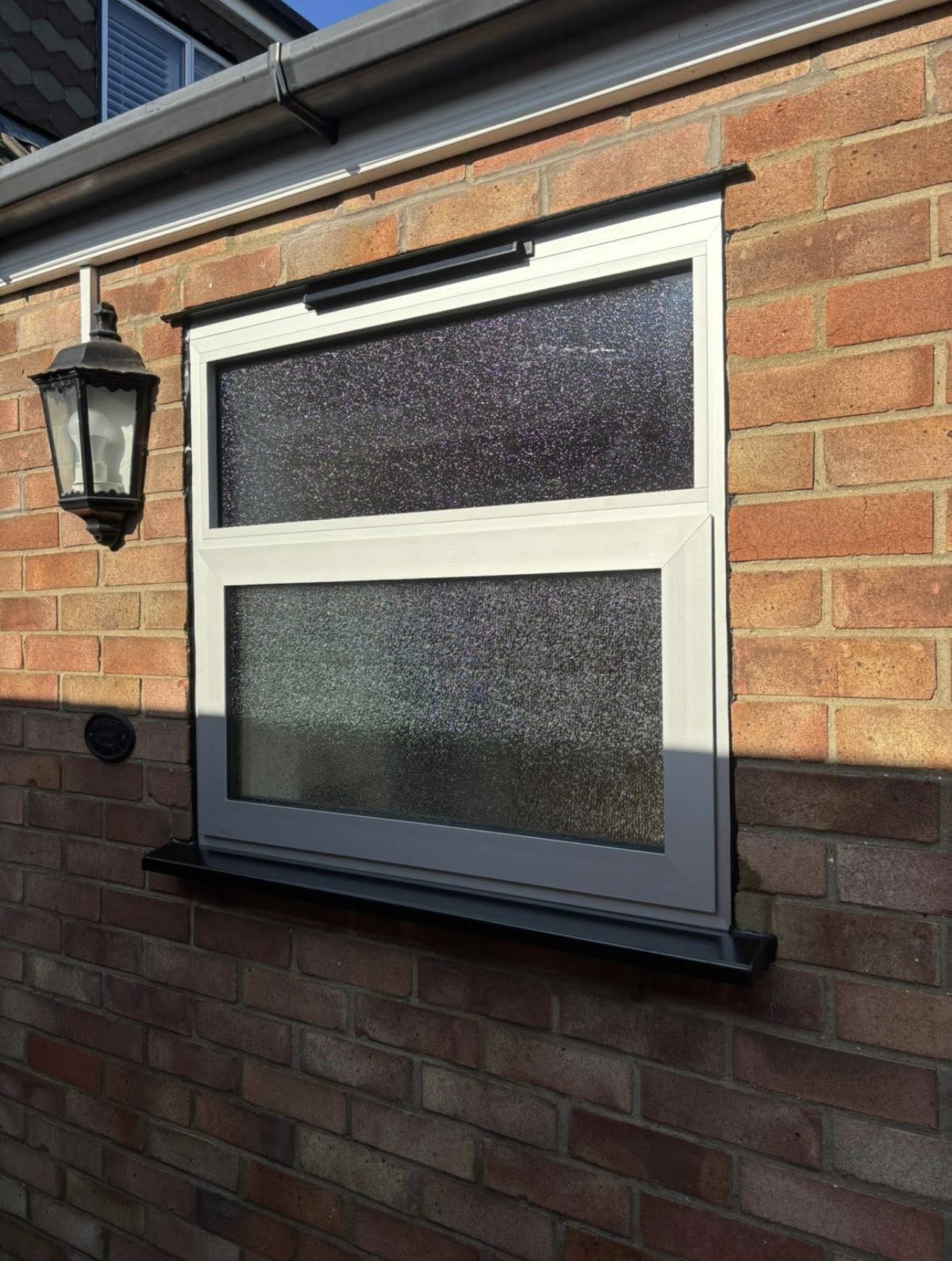 White tilt-and-turn window with obscure glass and black sill on a brick wall